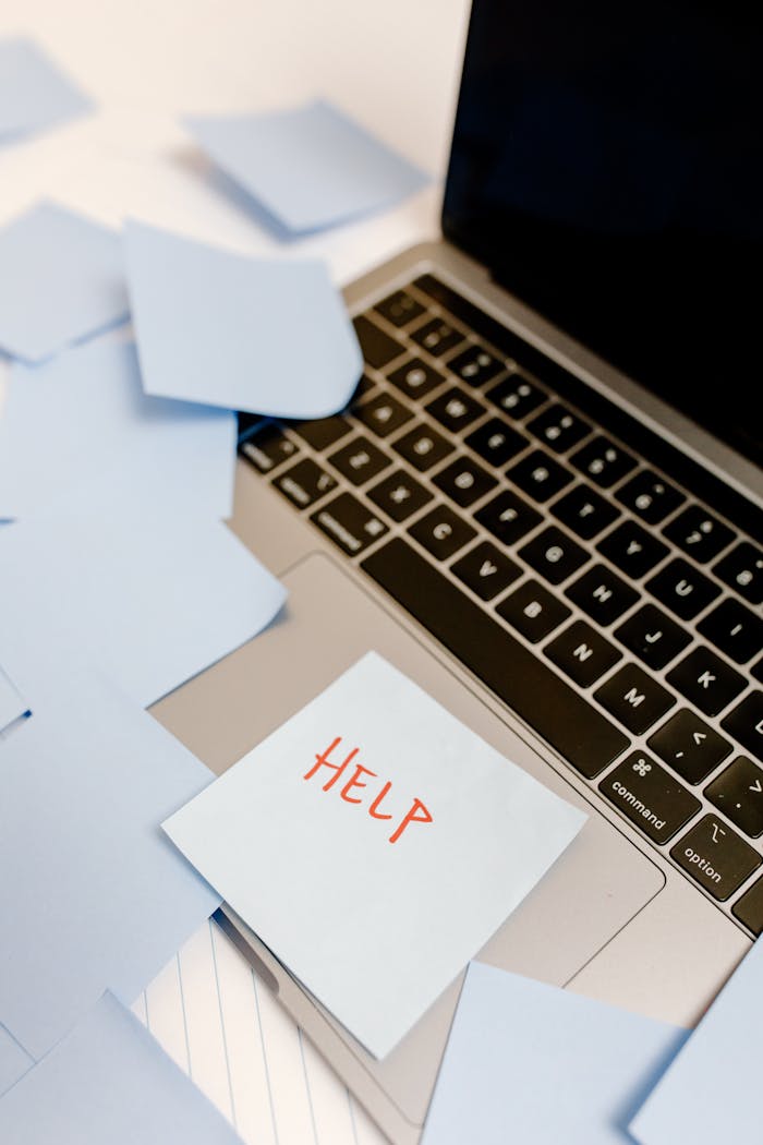 A laptop covered with sticky notes and a prominent Help sign, conveying urgency.