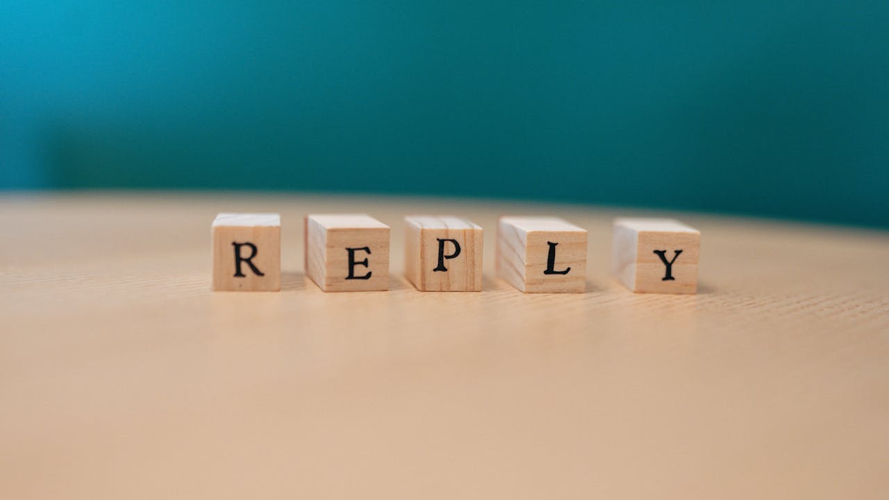 Close-up of wooden blocks spelling REPLY on a table with teal background.